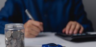 Autofinanzierung leicht gemacht: Exklusive Vorteile für ARCD-Mitglieder bei der PSD Bank West Auf einem Tisch steht ein Einmachglas gefüllt mit Geldmünzen, daneben ein kleines blaues Spielzeugauto auf ein paar weiteren Münzen