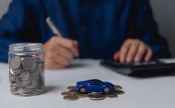 Autofinanzierung leicht gemacht: Exklusive Vorteile für ARCD-Mitglieder bei der PSD Bank West Auf einem Tisch steht ein Einmachglas gefüllt mit Geldmünzen, daneben ein kleines blaues Spielzeugauto auf ein paar weiteren Münzen