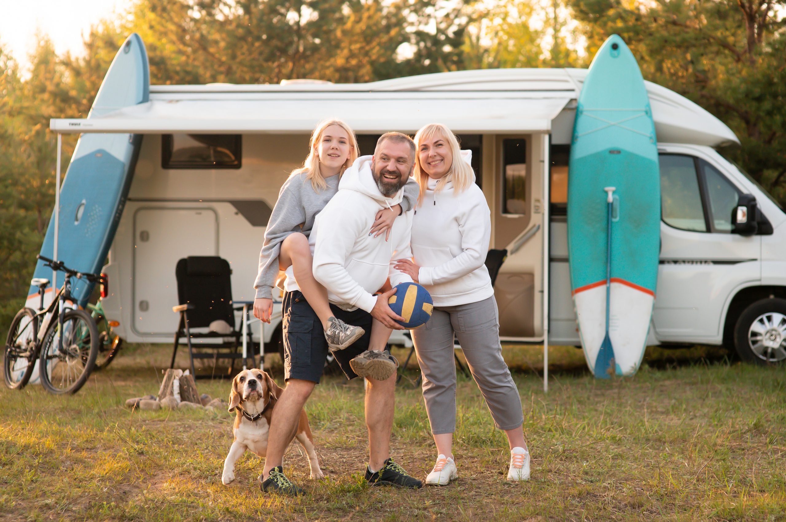 Happy parents with their child playing with a ball near their mobile home in the woods Vater, Mutter, Tochter und Hund stehen gut gelaunt vor ihrem Wohnmobil