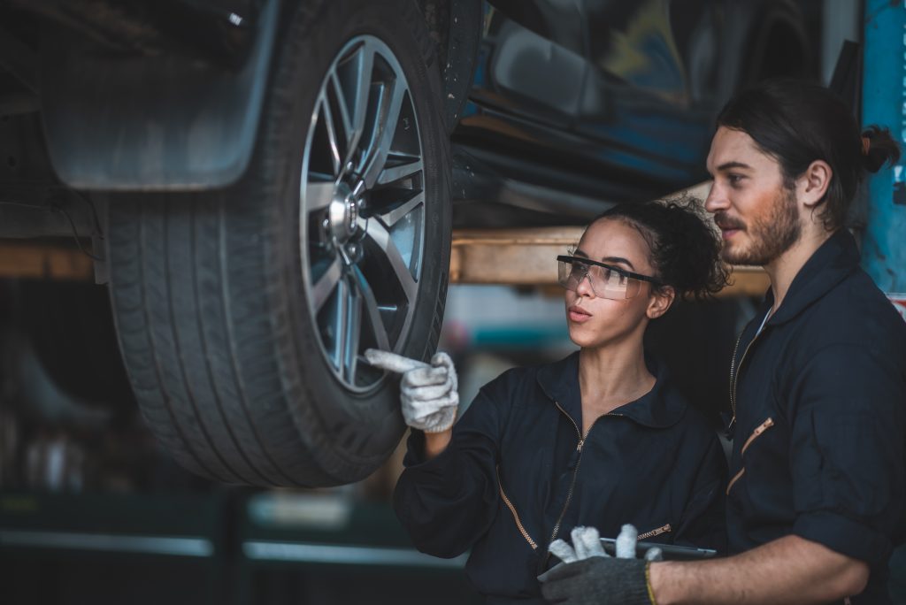 Ein weiblicher und ein männlicher Automechaniker prüfen den Reifen an einem aufgebockten Fahrzeug