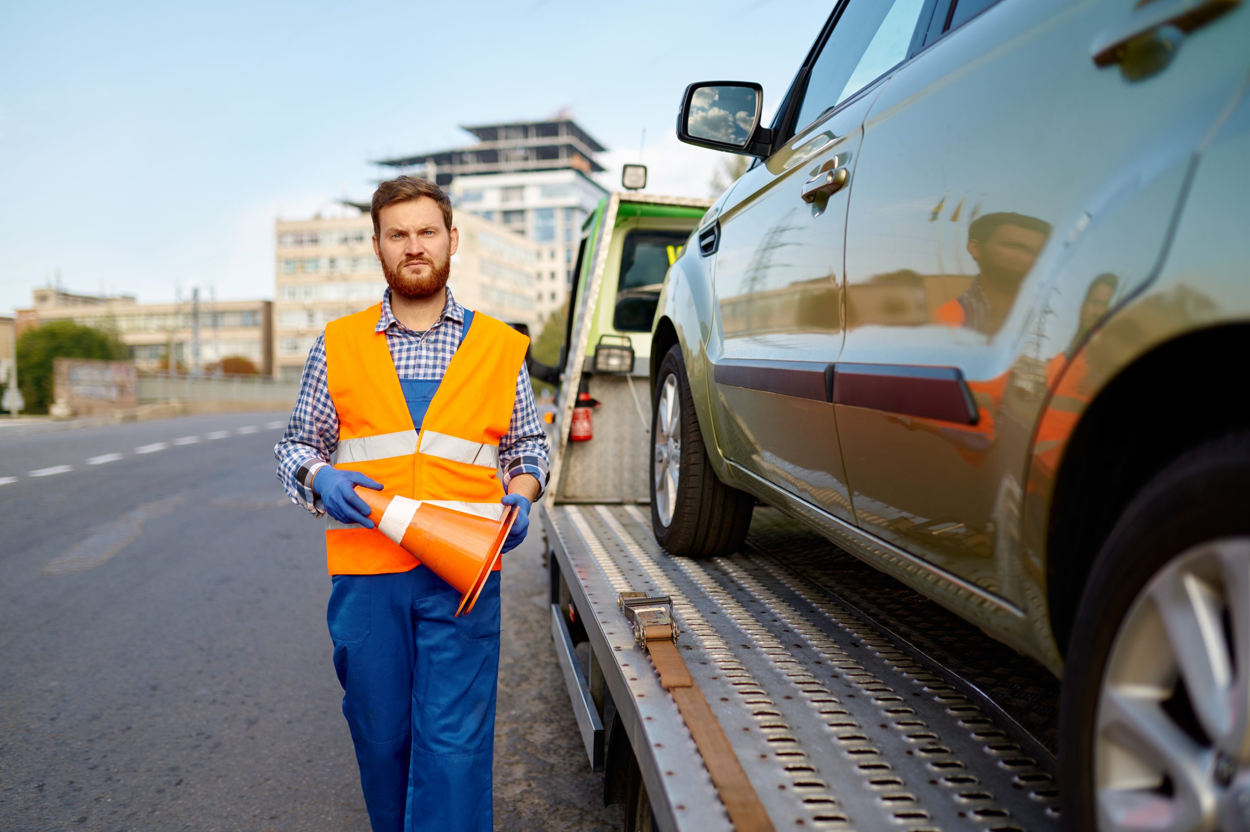 Road worker putting traffic cone on roadside Ein Pannenhelfer mit Warnweste sichert ein abgeschlepptes Auto auf dem Transporter